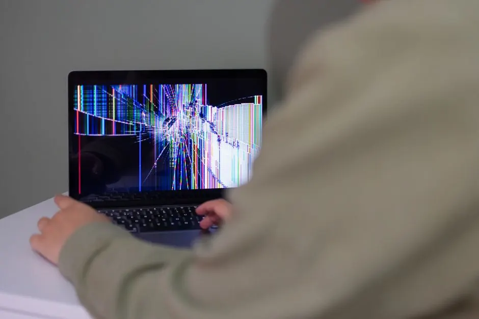 A person interacts with a laptop that has a cracked and distorted screen.