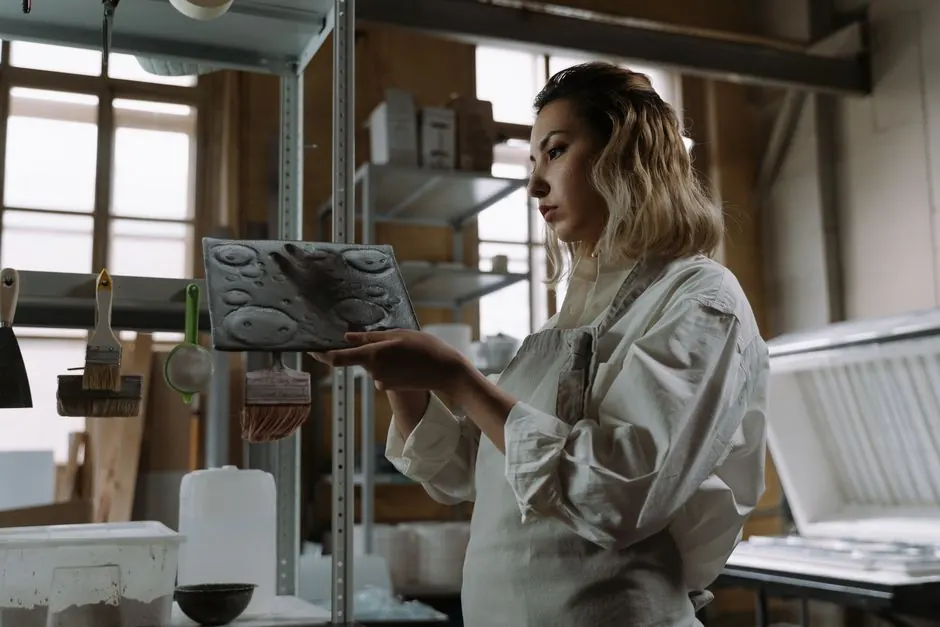 Craftswoman in apron examining ceramic molds in workshop, highlighting artistry and focus.